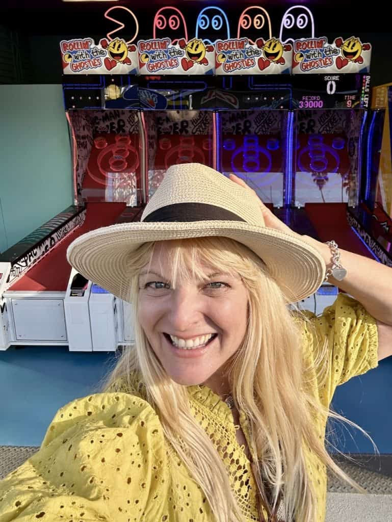 Kate Dana smiles in front of a row of Pac-Man skeeball machines, photo @katedana